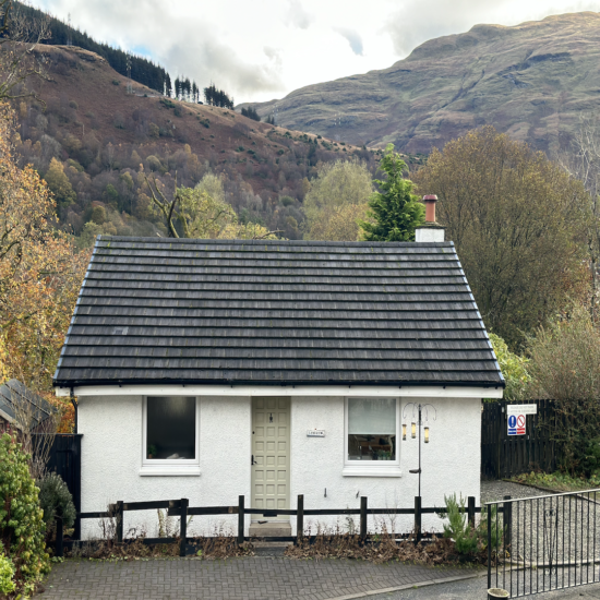 Exterior view of Langview Cottage, a charming white single-storey staycation property near Loch Long and Loch Lomond, surrounded by lush greenery and peaceful natural landscapes.