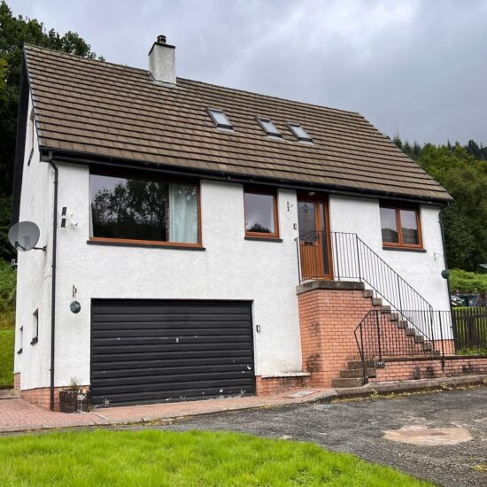 Exterior view of Wilmar Lodge, a charming white two-storey staycation property near Loch Long and Loch Lomond, surrounded by lush greenery and peaceful natural landscapes.